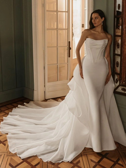 ÉLYSÉE Bridal HEIDI luxury satin Mikado fit-and-flare wedding dress featuring a sculpted strapless neckline, Basque waist, detachable tulle overskirt and cathedral train.
