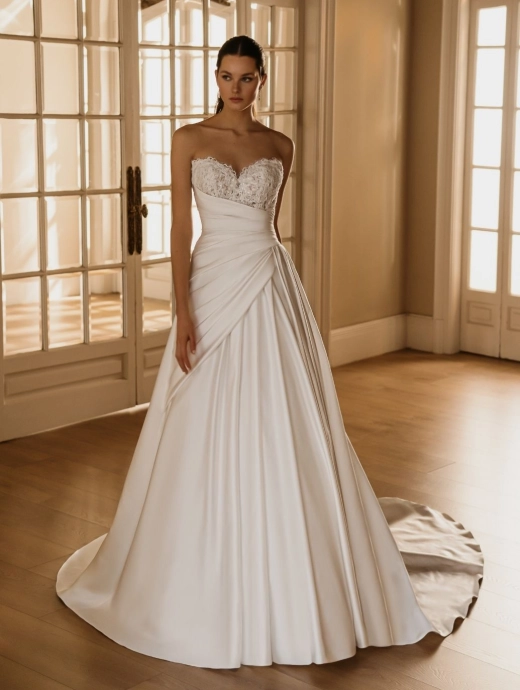 HERMIONE by ÉLYSÉE is a romantic A-line wedding dress featuring a sparkling embellished sweetheart bodice, softly draped satin skirt, and elegant cathedral train.